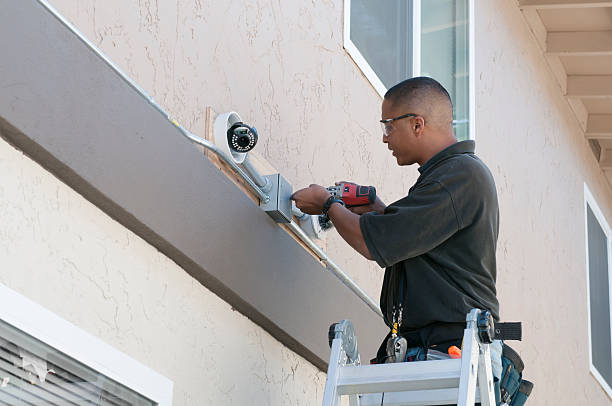 A technician installing a security camera system to the exterior of a building.Click below for more in this series: