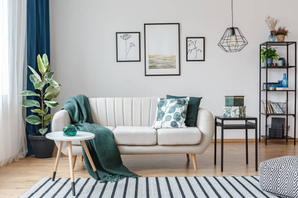 Black table next to sofa with green blanket in cozy apartment interior with gallery of posters