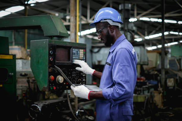African american factory worker in using  laptop and push buttons to test the machine operation after maintenance.