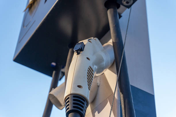 An electric vehicle charging station displays a charging handle. Clear blue sky is visible in the background, indicating it is daytime and sunny.