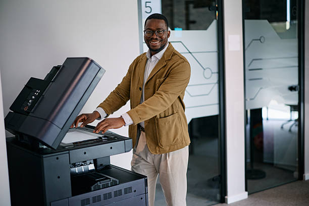 Cheerful African American manager using a multifunctional printer in a modern office, efficiently handling paperwork and administrative tasks with a positive attitude