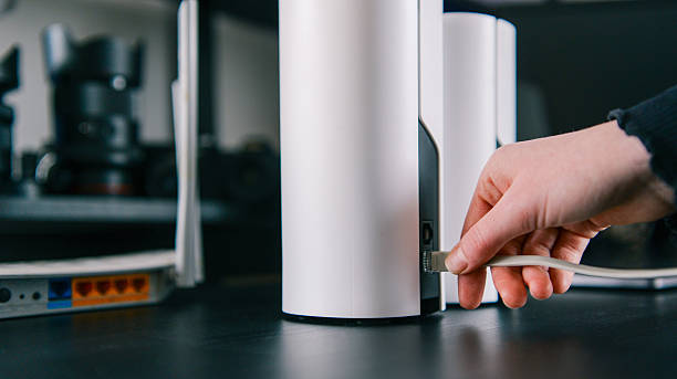 A person's hand inserts an Ethernet cable into a sleek, white mesh Wi-Fi node, suggesting network setup or expansion