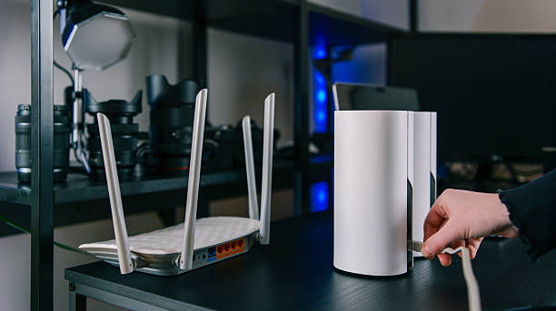 A person's hand connects a cable to a sleek white mesh Wi-Fi satellite unit next to a traditional router on a desk